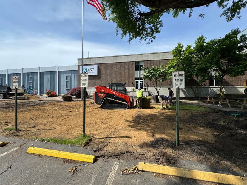 Construction site with heavy equipment and workers preparing landscaping near ASC building.