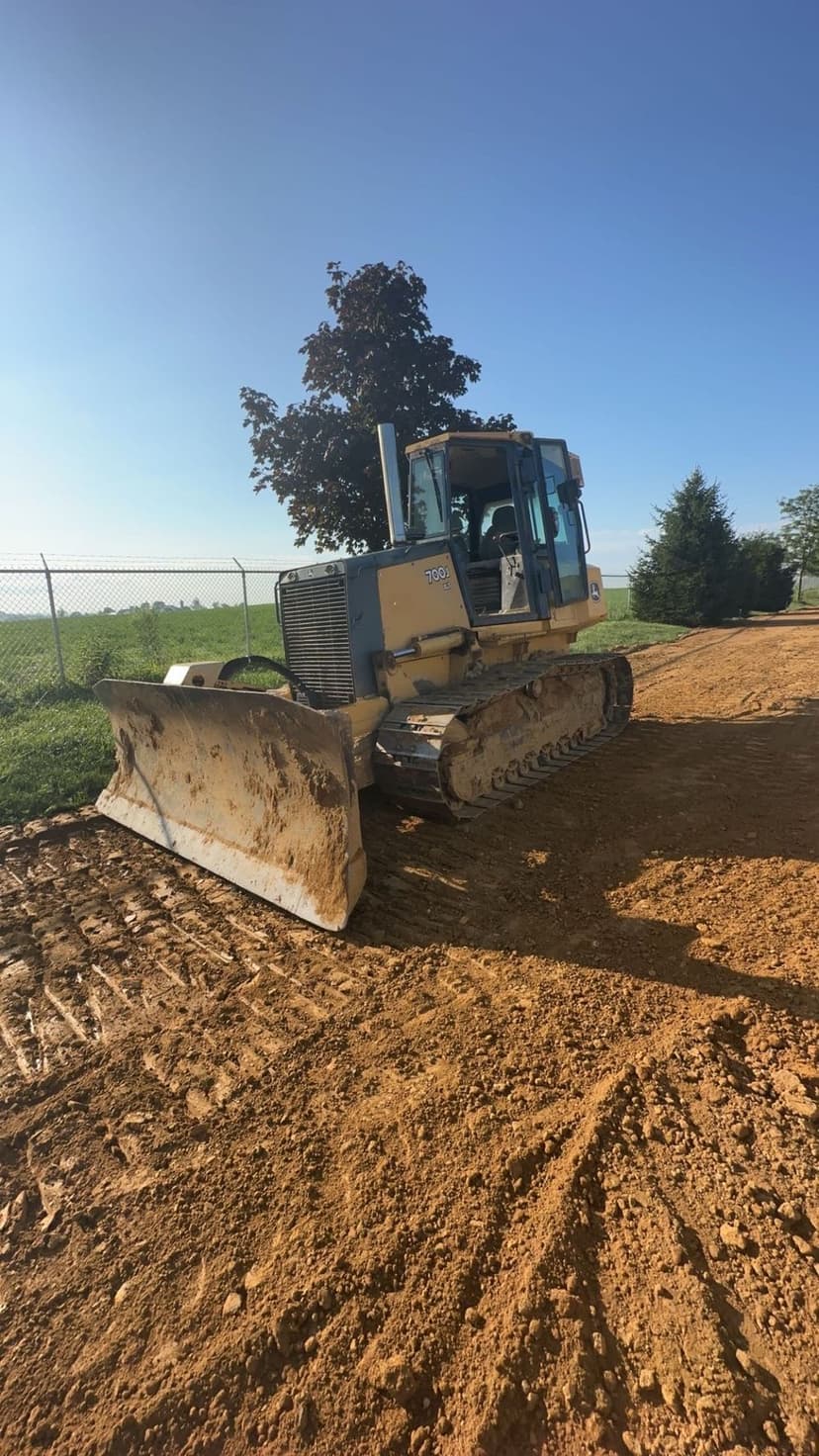 Bulldozer on dirt site with clear blue sky and green landscape in background.