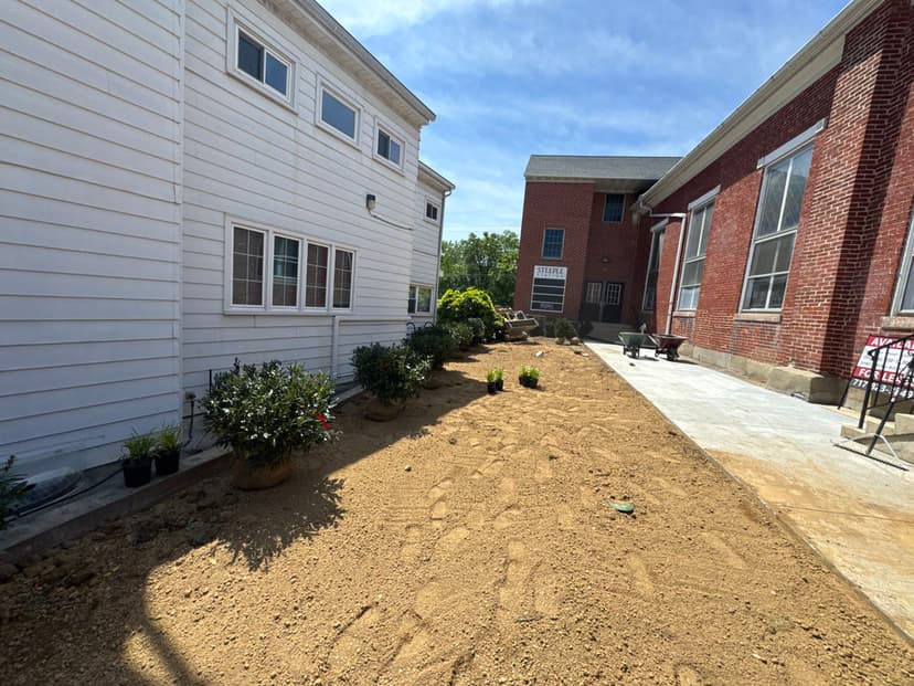 Side yard renovation with freshly tilled soil and planting area between two buildings.