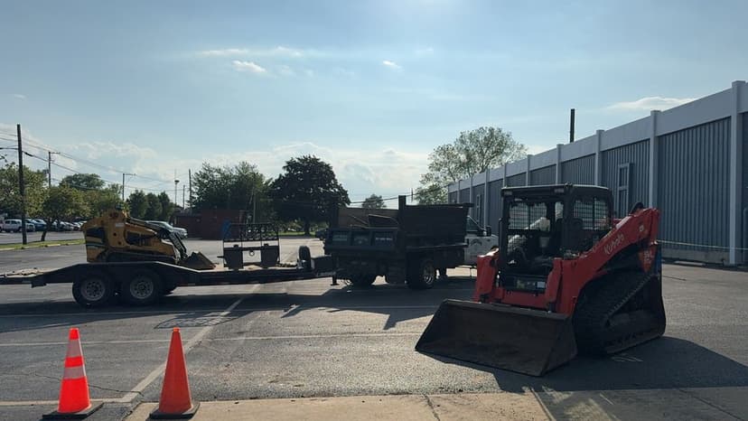 Red Bobcat skid steer and yellow mini excavator on flatbed trailer at construction site.
