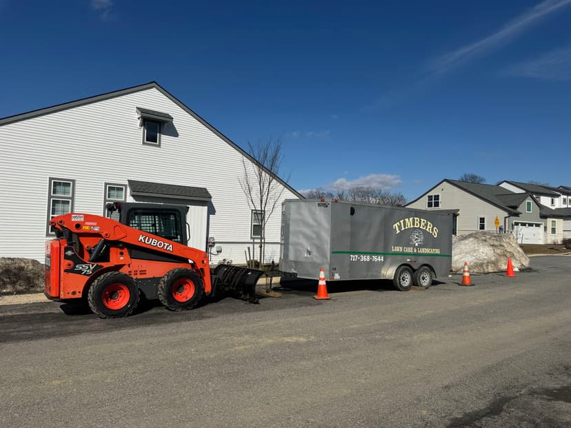 Kubota loader and Timbers lawn care trailer parked on residential street on sunny day.