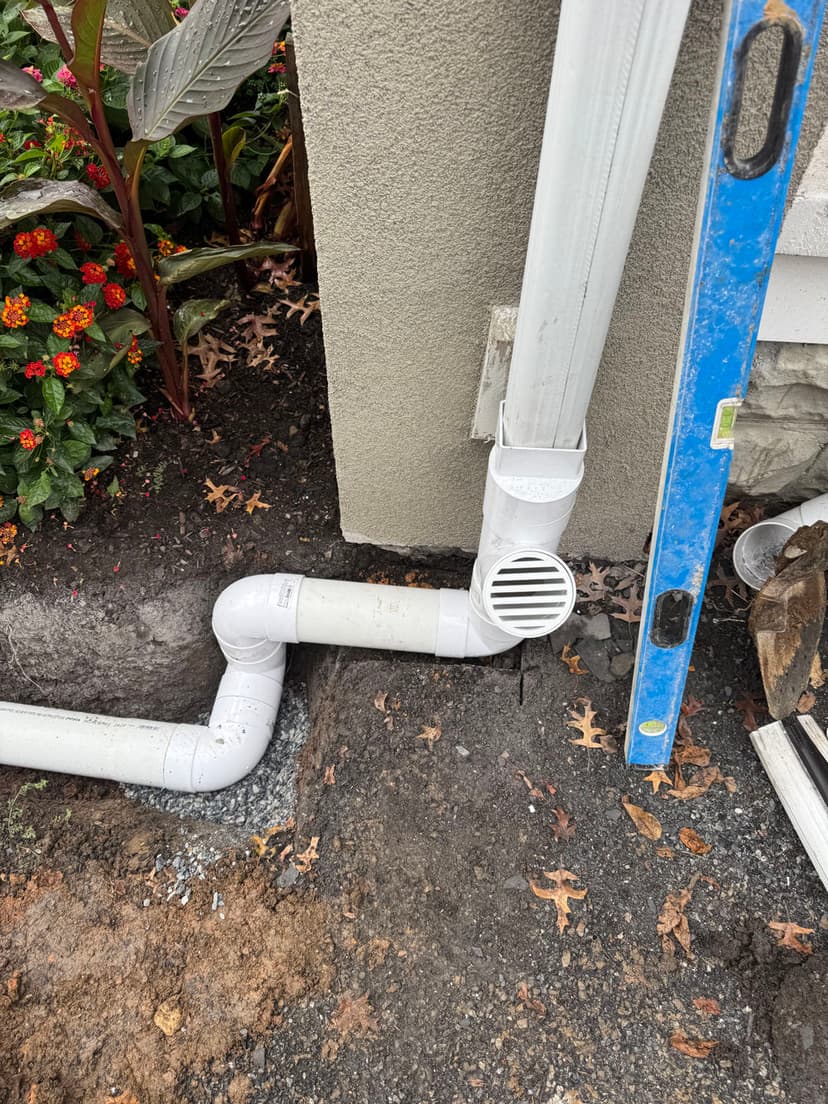 Downspout drainage system connected to a home, surrounded by landscaping and tools.