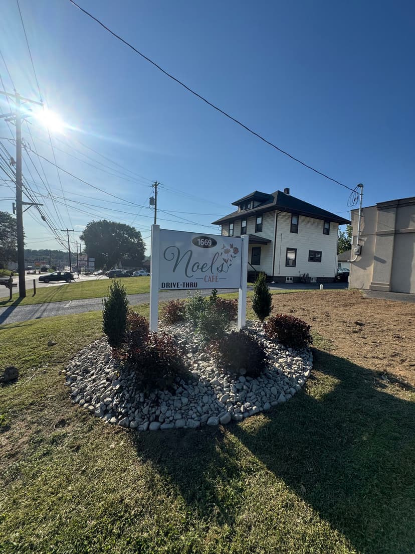 Sign for Noel's Drive-Thru Café at 1669, featuring landscaping and clear sky backdrop.
