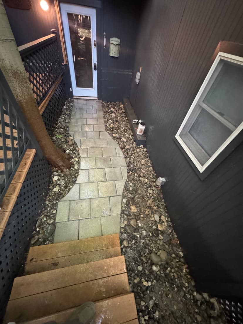 Paved pathway leading to a side entrance, bordered by rocks and trees. Outdoor lighting visible.