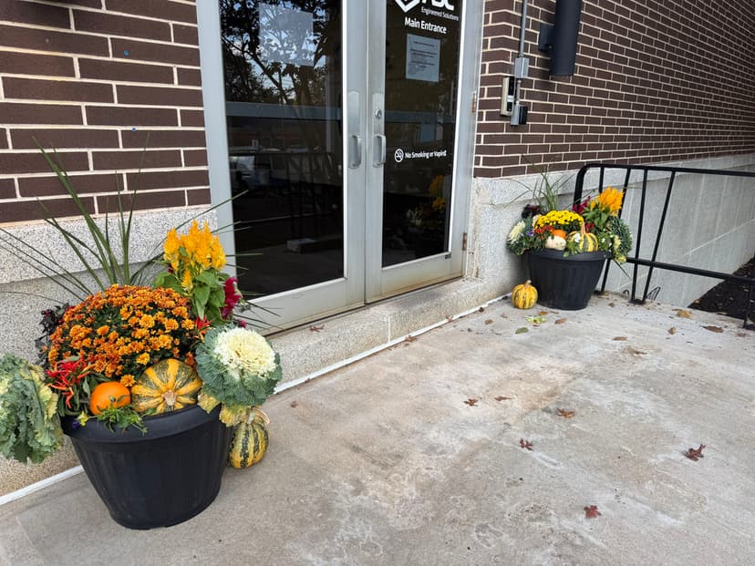 Colorful fall planters with pumpkins, gourds, and flowers at building entrance.