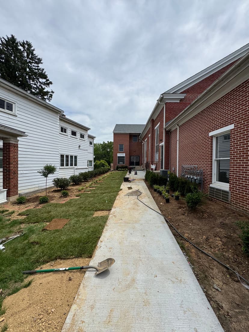 Construction site featuring a newly paved walkway between two brick buildings and landscaping work.