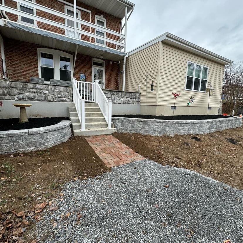 Home exterior featuring a landscaped yard, stone retaining wall, and brick pathway to entrance.