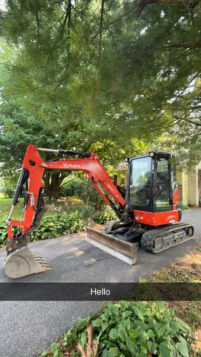 Kubota mini excavator parked on a driveway surrounded by greenery.